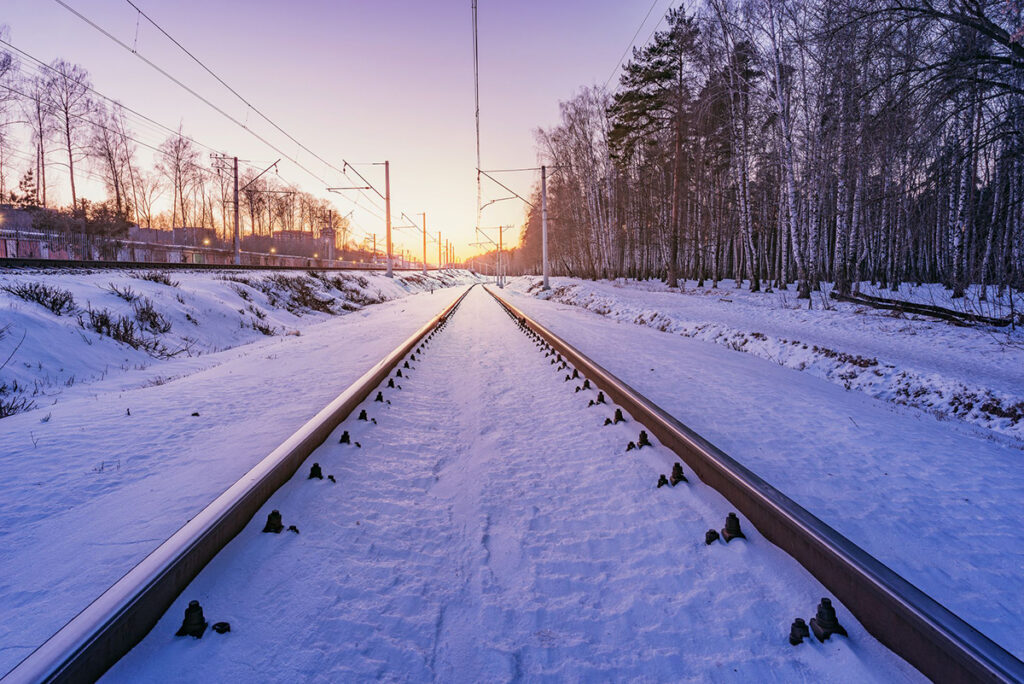 Train tracks covered in snow and overhead electrical wires, facing towards the horizon.