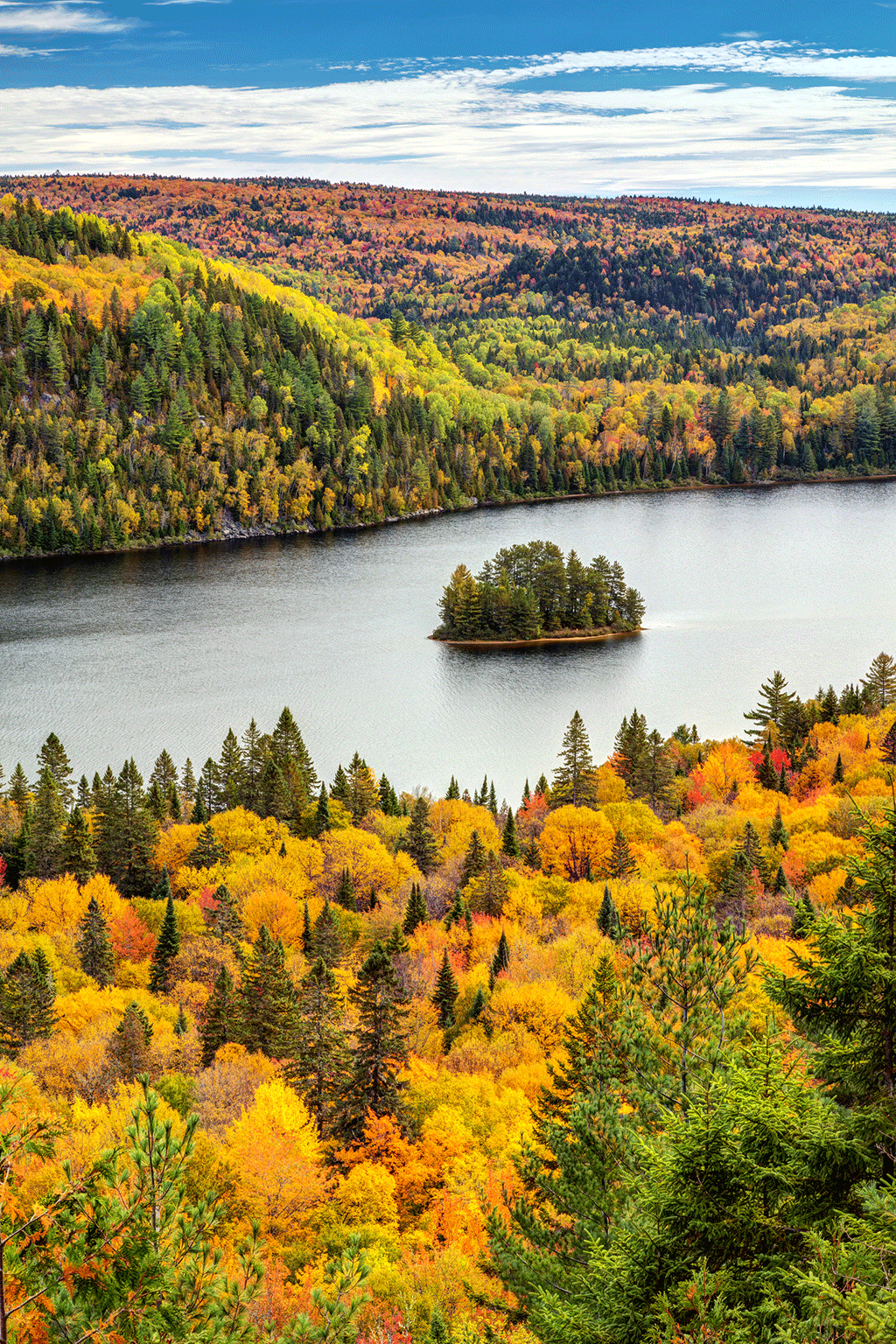 Île dans une rivière avec des forêts des deux côtés d'un plan d'eau. Les arbres changent de couleur à l'automne.